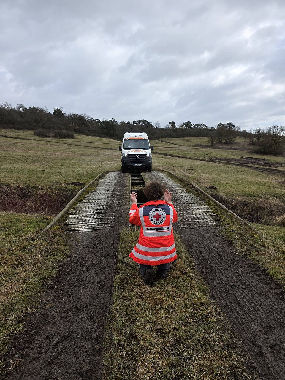 ein KTW-B ZS wird zur Fahrt über eine Behelfsbrücke eingewiesen, hin Hintergrund das leicht wellige wenig bewachsene Gelände des Standort-Übungsplatzes Fritzlar