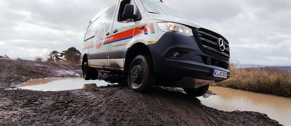 im Gelände: der Zivilschutz Krankentransportwagen (KTW B-ZS) diagonal auf 2 Rädern balancierend im schlammigen Gelände auf einem kleinen Geländebuckel
